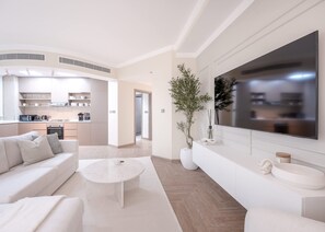 A modern living room with a sofa, coffee table, and a TV. The room has a kitchen in the background with cabinets and appliances. - Stayshort - 2 Bedroom in Dubai Marina With Huge Balcony (Dubai)