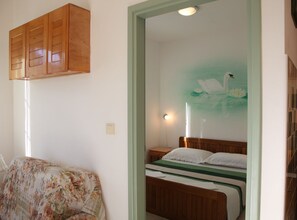 Ein Schlafzimmer mit einem hölzernen Bett, einer blumigen Tagesdecke, einem wandmontierten Schrank und einem Schwandaffiche.