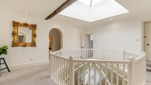 Een ruime kamer met een hoge plafond, dakraam, een wit kinderbedje, een spiegel en een trap.