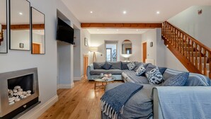 A living room with a fireplace, a sofa, a coffee table, and a TV. - 3 Bed in Tenby (oc-t30644) (Tenby)