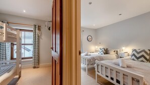 A bedroom with bunk beds, a window with curtains, a bedside table with a lamp, and a wall clock. - 3 Bed in Tenby (oc-t30644) (Tenby)