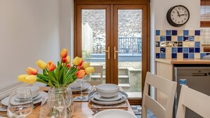 A dining area with a table set for four, a vase of tulips, and a clock on the wall. - 3 Bed in Tenby (oc-t30644) (Tenby)