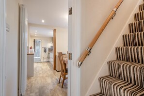 Un escalier recouvert d’une moquette à rayures menant à un palier, une chaise en bois et, au fond, un coin cuisine.