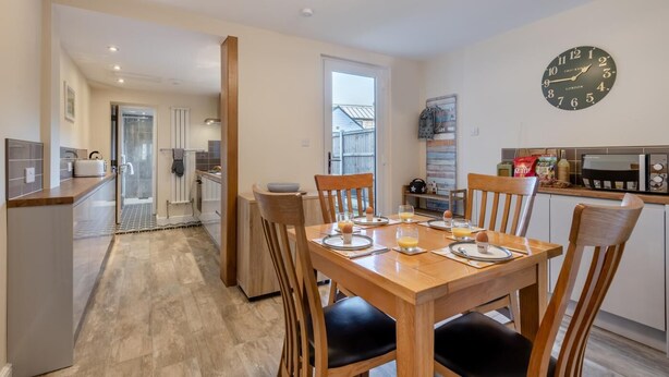 A modern kitchen with a dining area, a large wall clock, and a view of the outside. - 2 Bed in Sheringham (oc-h30635) (Sheringham)