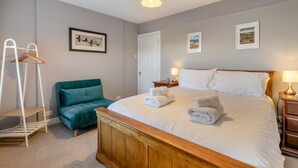 A bedroom with a bed, a wooden headboard, a teal sofa, a white hanging coat rack, and a door. - 2 Bed in Sheringham (oc-h30635) (Sheringham)