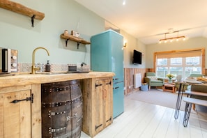 A kitchen with a wooden barrel, a teal refrigerator, and a dining area with a table and chairs. - 2 Bed in Eccles-on-Sea (oc-s30665) (Eccles-on-Sea)