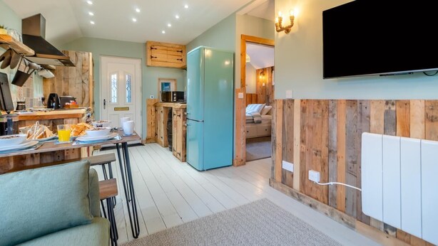 Eine moderne Küche mit Holzelementen, einem blauen Kühlschrank und einem an der Wand befestigten Flachbildfernseher.
