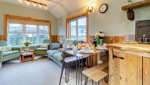 Ein gemütliches Zimmer mit einer Couch, Sesseln, einem Esstisch mit Frühstück und einer Küchenzeile.