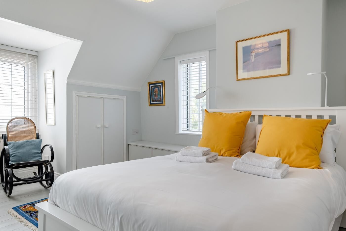 A bedroom with a large bed, two pillows, a chair, a desk, and a window.