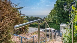 A staircase with metal railings leading to a road, surrounded by greenery and a view of the sea. - 2 Bed in Ventnor (oc-w30525) (Ventnor)