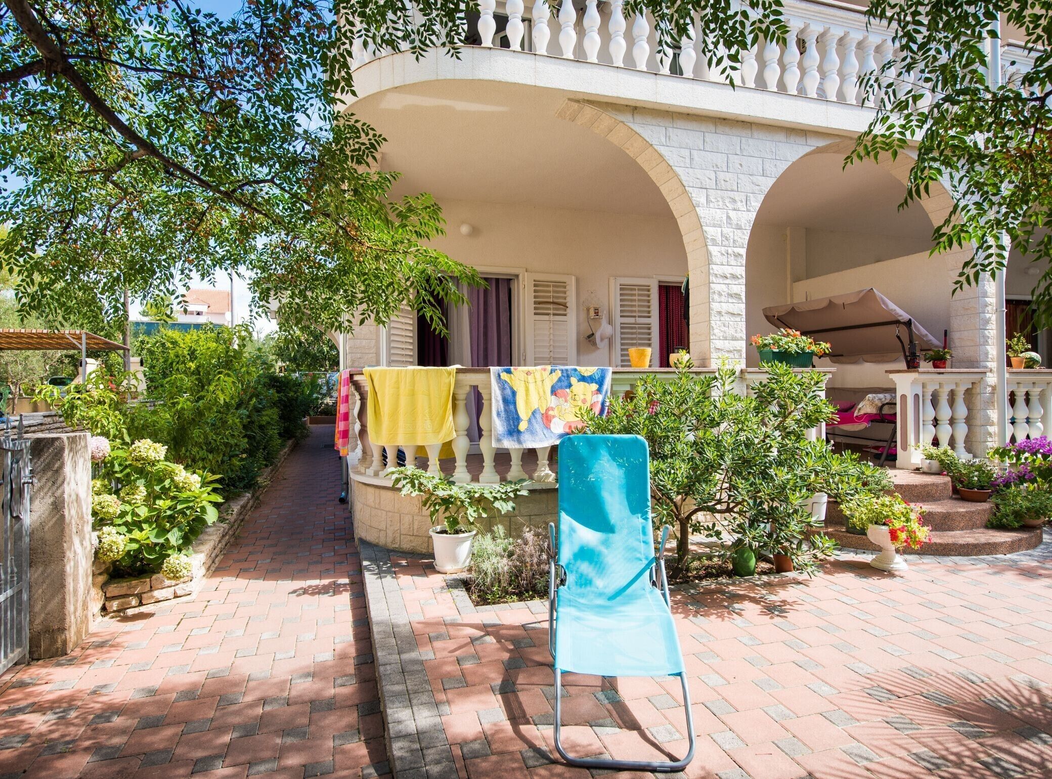 A courtyard with a covered seating area, a chair, and a balcony with a railing.