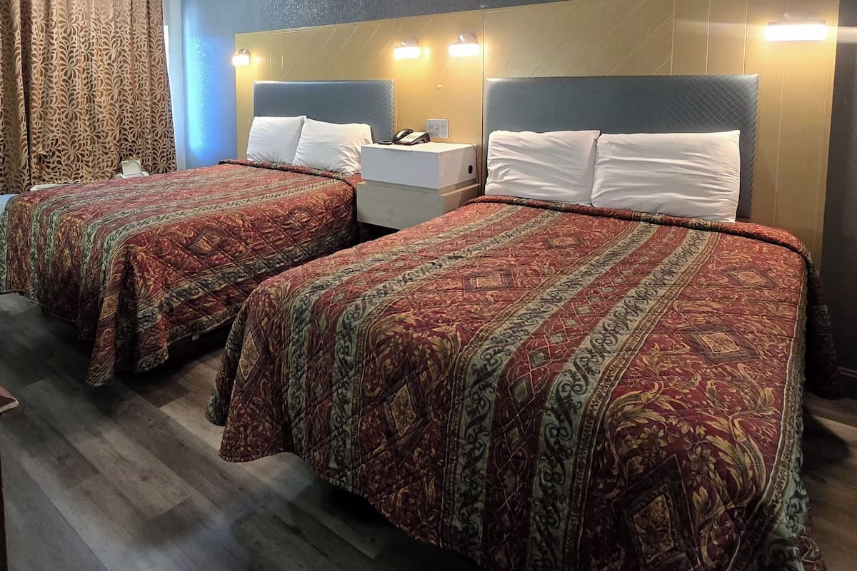 Habitación de hotel con dos camas, cada una con una colcha estampada, mesitas de noche con lámparas y cabeceros con iluminación integrada.