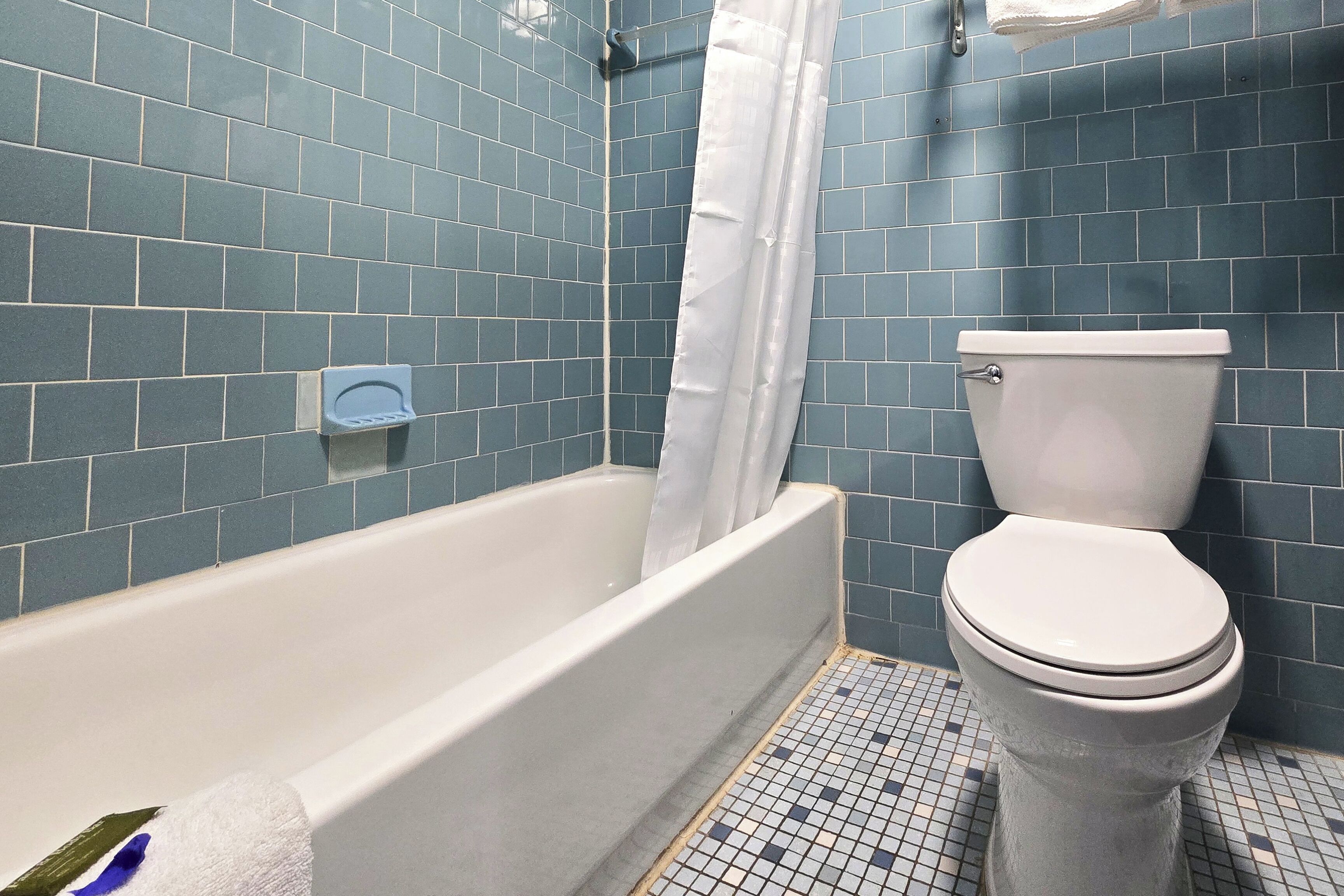 Een badkamer met een bad, toilet en blauwe betegelde wanden.