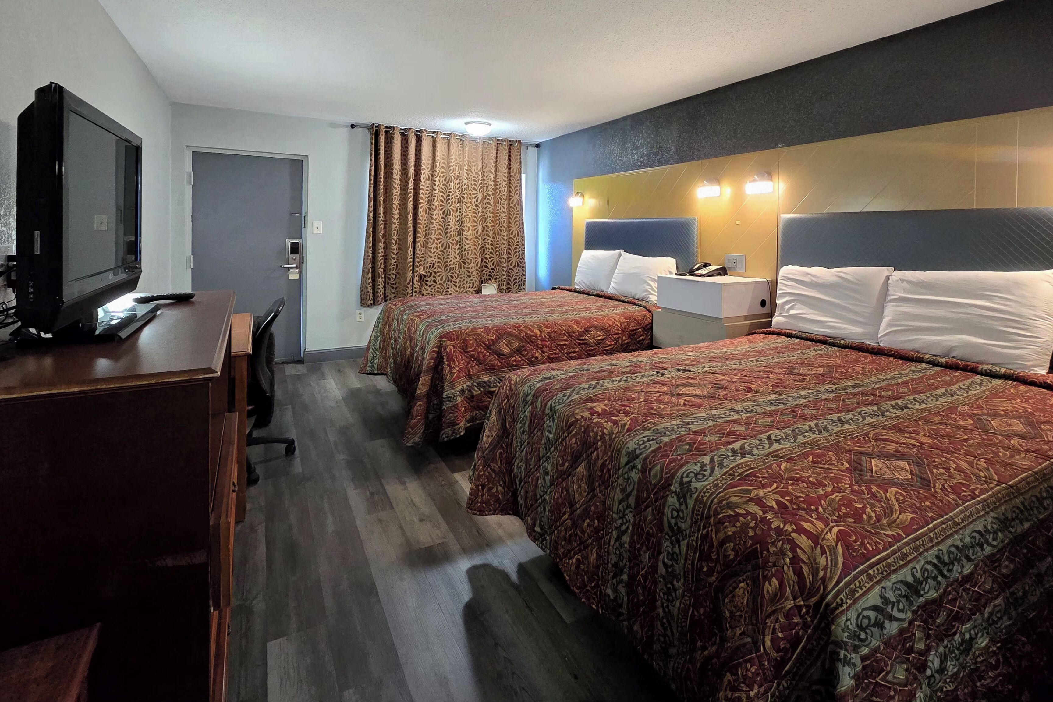 Ein Hotelzimmer mit zwei Betten, einem Schreibtisch mit Fernseher und einer Tür mit Vorhängen.