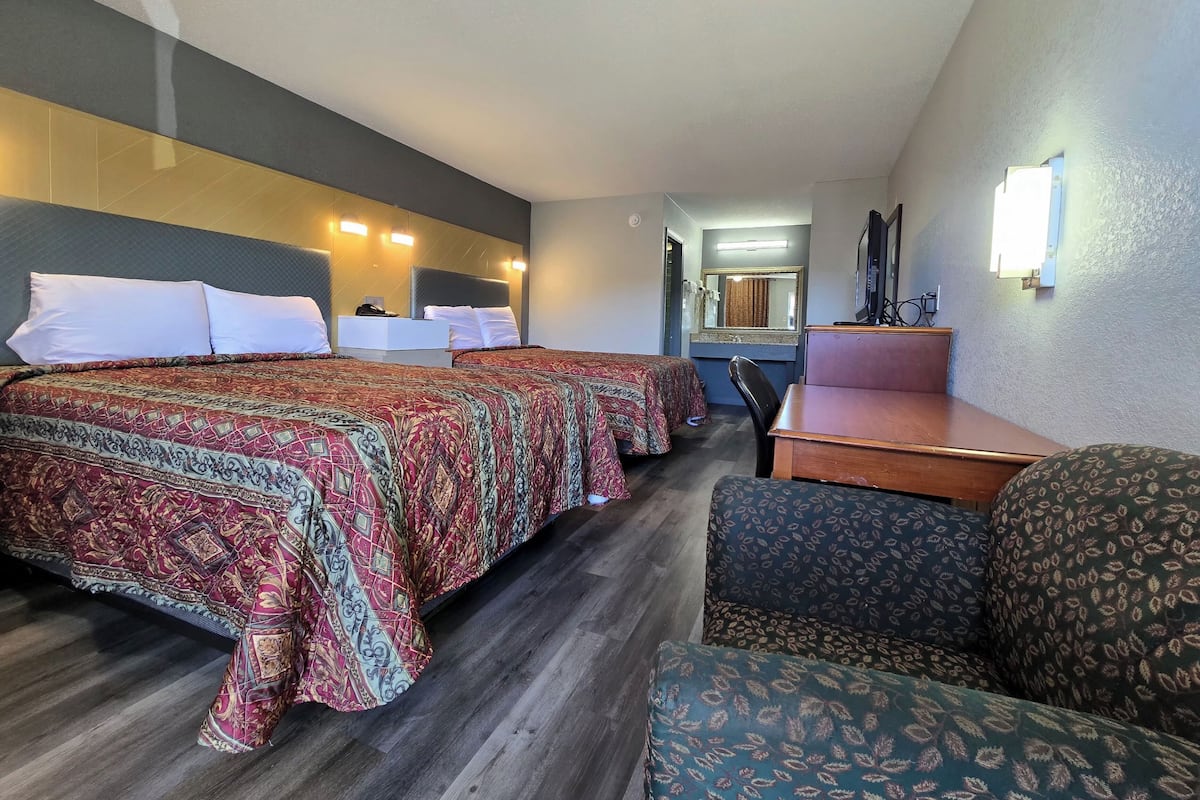 Una habitación de hotel con dos camas, un escritorio, una silla y un espejo.