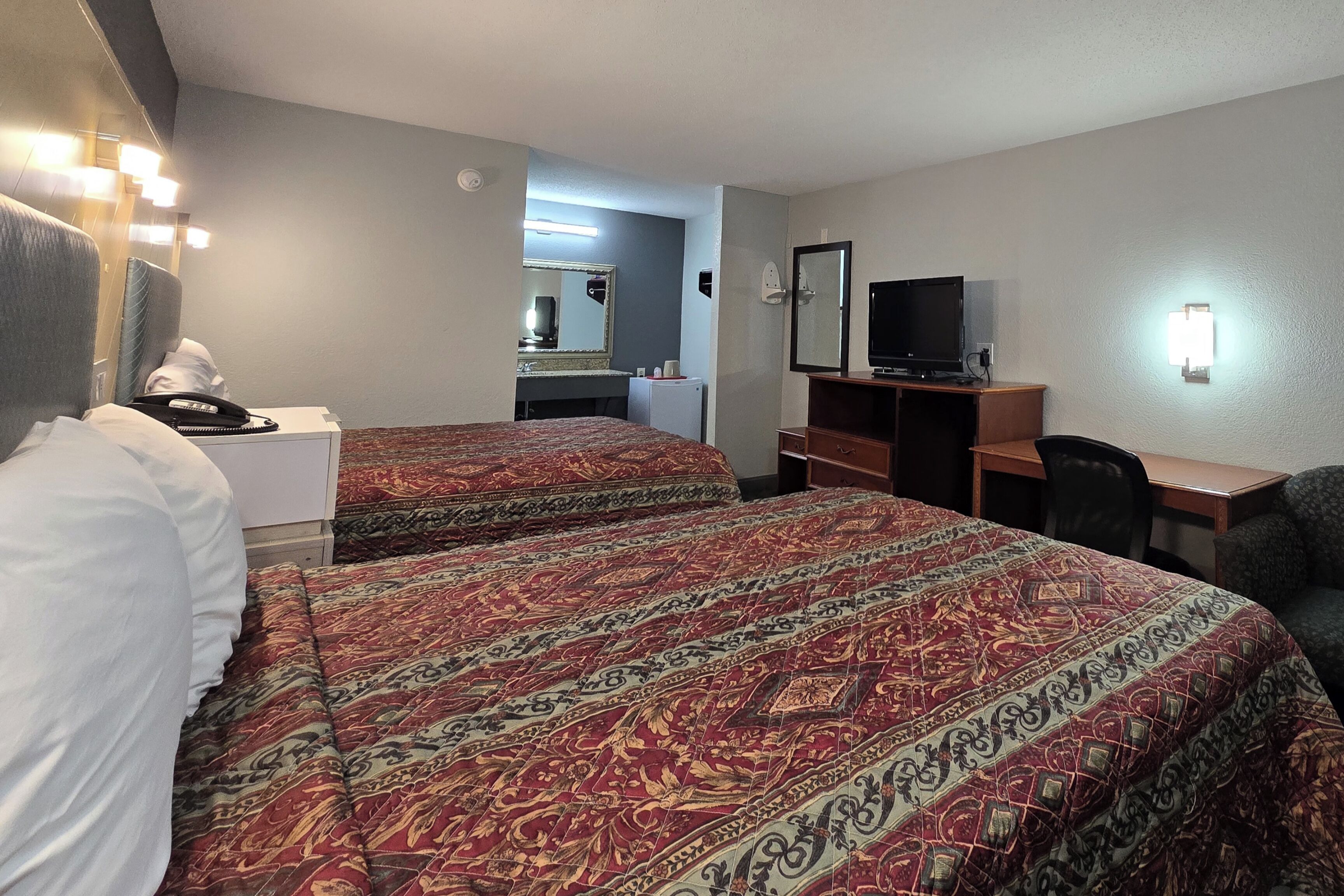 Una habitación de hotel con dos camas, un escritorio, una silla, un televisor y un espejo.