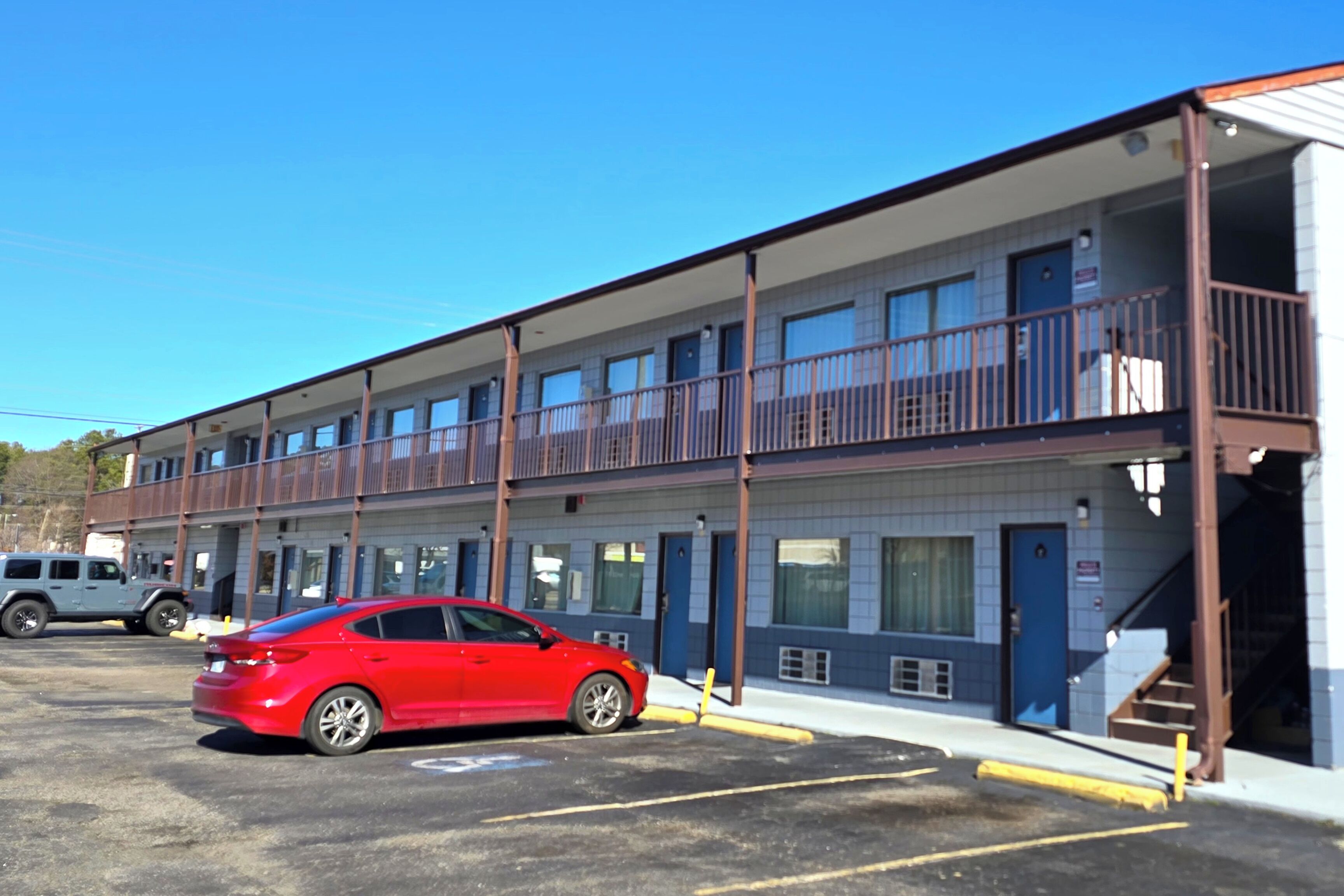 A multi-story motel with a red car parked in the lot.
