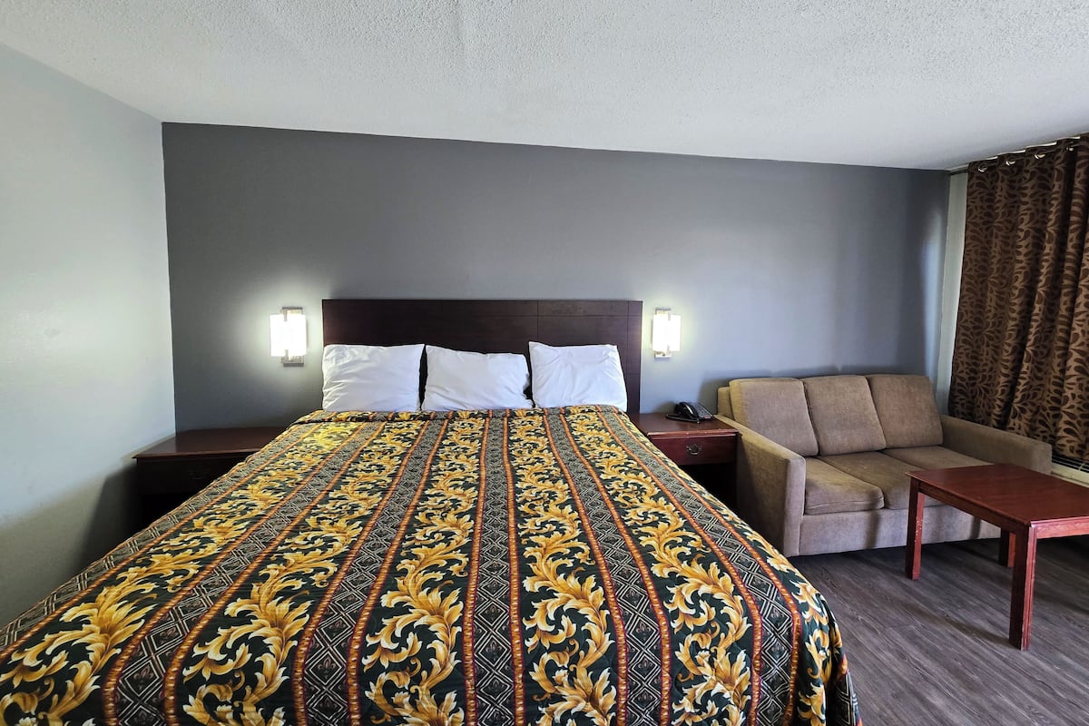 Una habitación de hotel con una cama grande, un sofá, una mesita y dos lámparas de noche.