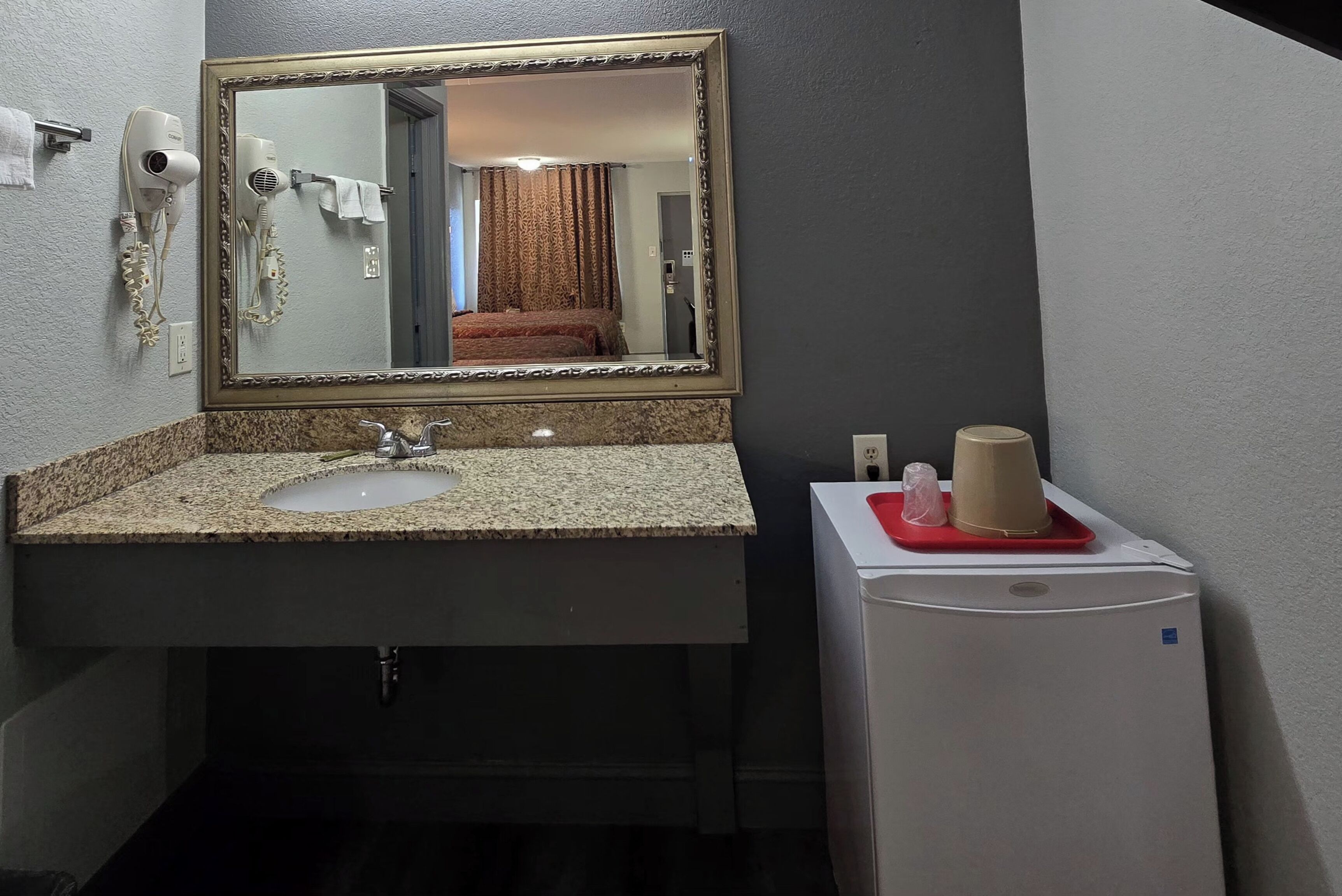 Une salle de bain équipée d’un lavabo, d’un miroir, d’un sèche-cheveux et d’un petit réfrigérateur.
