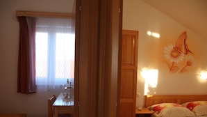 Ein Hotelzimmer mit Bett, Schreibtisch, Stuhl, einem Fenster mit Vorhängen und einer Wand mit einem floralen Gemälde.