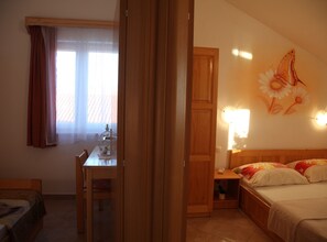 A hotel room with a bed, a desk, a chair, a window with curtains, and a wall with a floral painting. - Apartments Gabi - Two Bedroom/balcony/sea view(B3) (Srima)