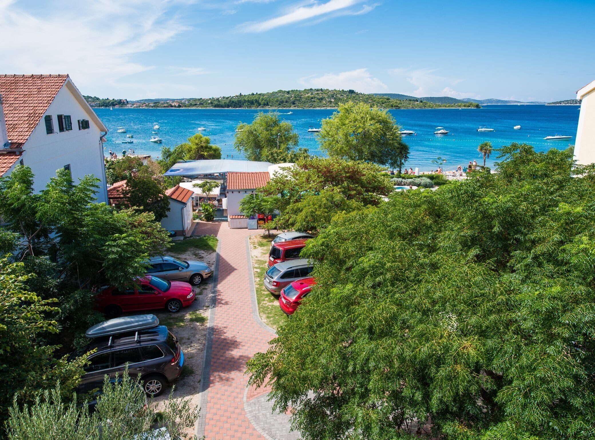 A coastal view with parked cars, a pathway, and a building with a red roof.