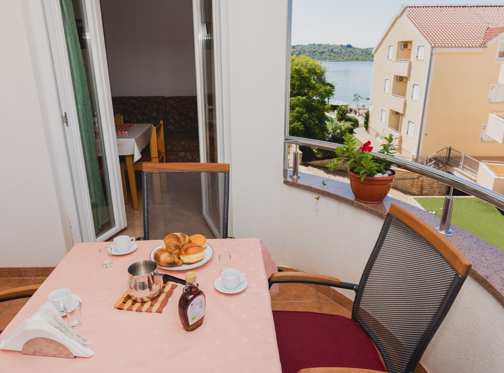 A balcony with a table set for breakfast, including croissants, a bottle of honey, and a teapot.