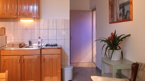 A compact kitchen with wooden cabinets, a gas stove, and a sink. There's a small trash bin and a potted plant on a side table. - Apartments Gabi - One Bedroom/balcony/sea view(B4) (Srima)