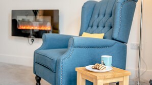 A blue upholstered armchair with a tufted backrest and decorative buttons, positioned in front of a flat-screen TV mounted on a white wall. - 2 Bed in Swanage (oc-w30658) (Swanage)