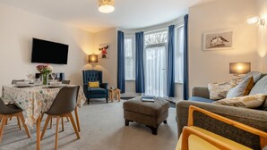A modern living room with a dining area, a blue armchair, a grey sofa, and a flat-screen TV mounted on the wall. - 2 Bed in Swanage (oc-w30658) (Swanage)