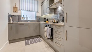 A modern kitchen with grey cabinets, a microwave, a stove, and a window with blinds. - 2 Bed in Swanage (oc-w30658) (Swanage)