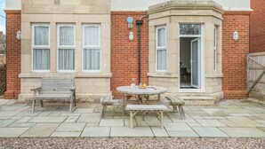A two-story house with a patio area featuring a wooden bench, a round table, and a small garden. - 2 Bed in Swanage (oc-w30658) (Swanage)