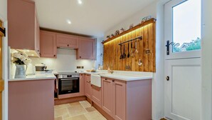 Une cuisine compacte avec des meubles de couleur rose, un pare-feu en bois et un four encastré.