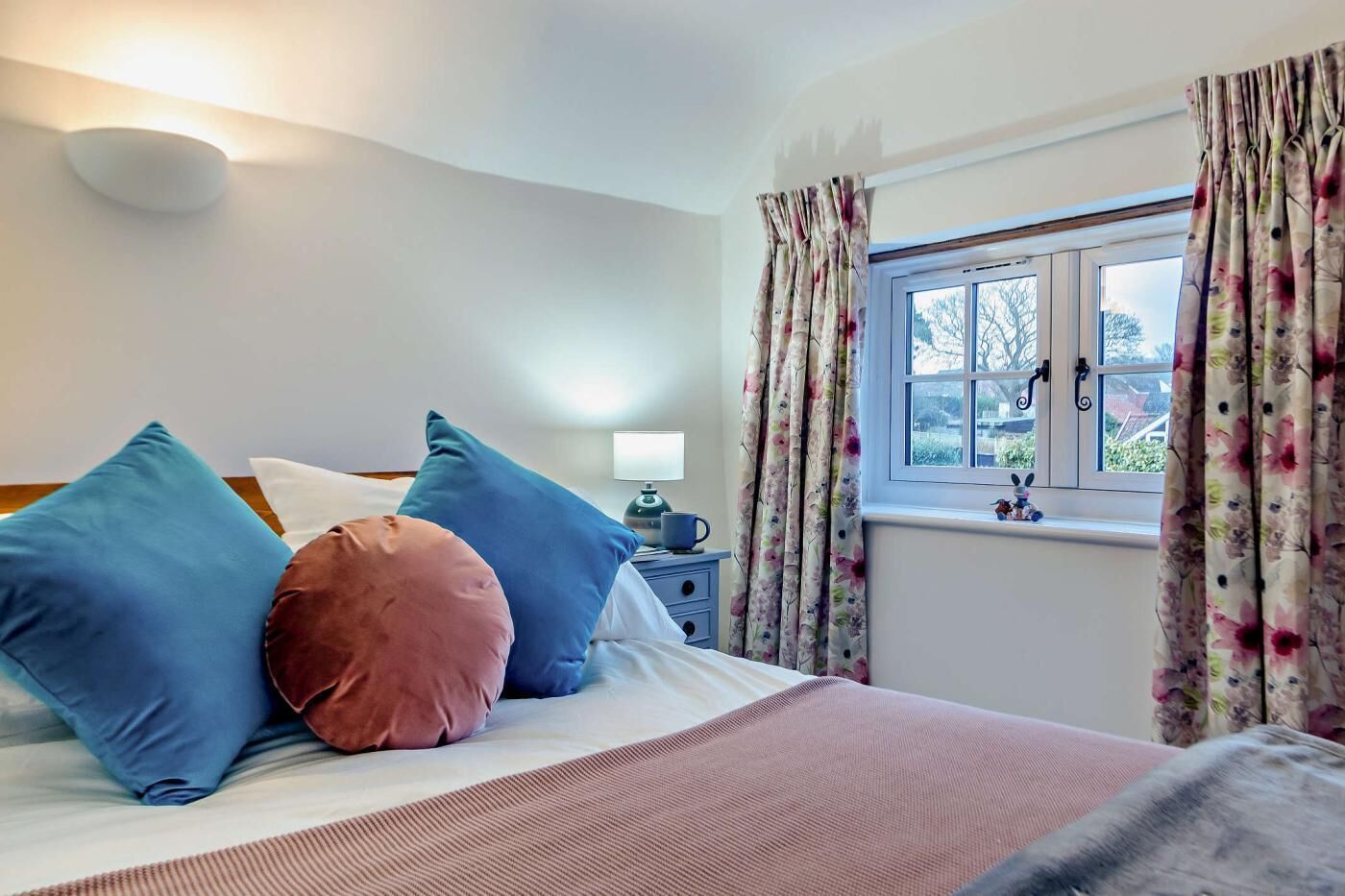 A bedroom with a bed, pillows, a nightstand, a lamp, and a window with curtains.