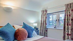 Une chambre à coucher avec un lit, des oreillers, une table de chevet, une lampe et une fenêtre avec des rideaux.