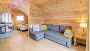 A cozy cabin interior with a wooden ceiling, a gray sofa with yellow cushions, a small kitchen area, and a bed with a yellow blanket. - 1 Bed in East Cowton (oc-w30480) (East Cowton)