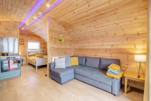 A cozy cabin interior with a wooden ceiling, a gray sofa with yellow cushions, a small kitchen area, and a bed with a yellow blanket. - 1 Bed in East Cowton (oc-w30480) (East Cowton)