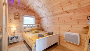 A cozy wooden cabin bedroom with a bed, bedside lamp, and a window.