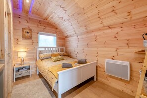 A cozy wooden cabin bedroom with a bed, bedside lamp, and a window.