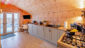 Una cocina acogedora de estilo cabaña, con techo de madera, estufa integrada y una puerta corrediza de vidrio que da a un área exterior con patio y sillas.