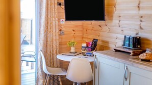 Una habitación acogedora de estilo cabaña, con interior de madera, una mesa de comedor con sillas, una pequeña cocina con un tostador y un televisor montado en la pared.