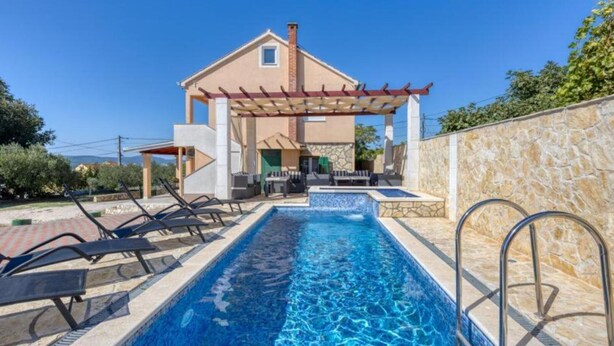Una casa de dos pisos con piscina, mobiliario de exterior y una pérgola.