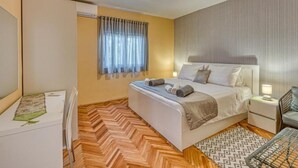 Habitación de hotel con cama, mesita de noche, silla, alfombra estampada y suelo de madera con dibujo de espiga.