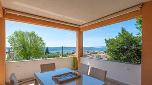 Un balcón con una mesa de vidrio y sillas de mimbre, con vistas panorámicas a un pueblo costero y al mar.