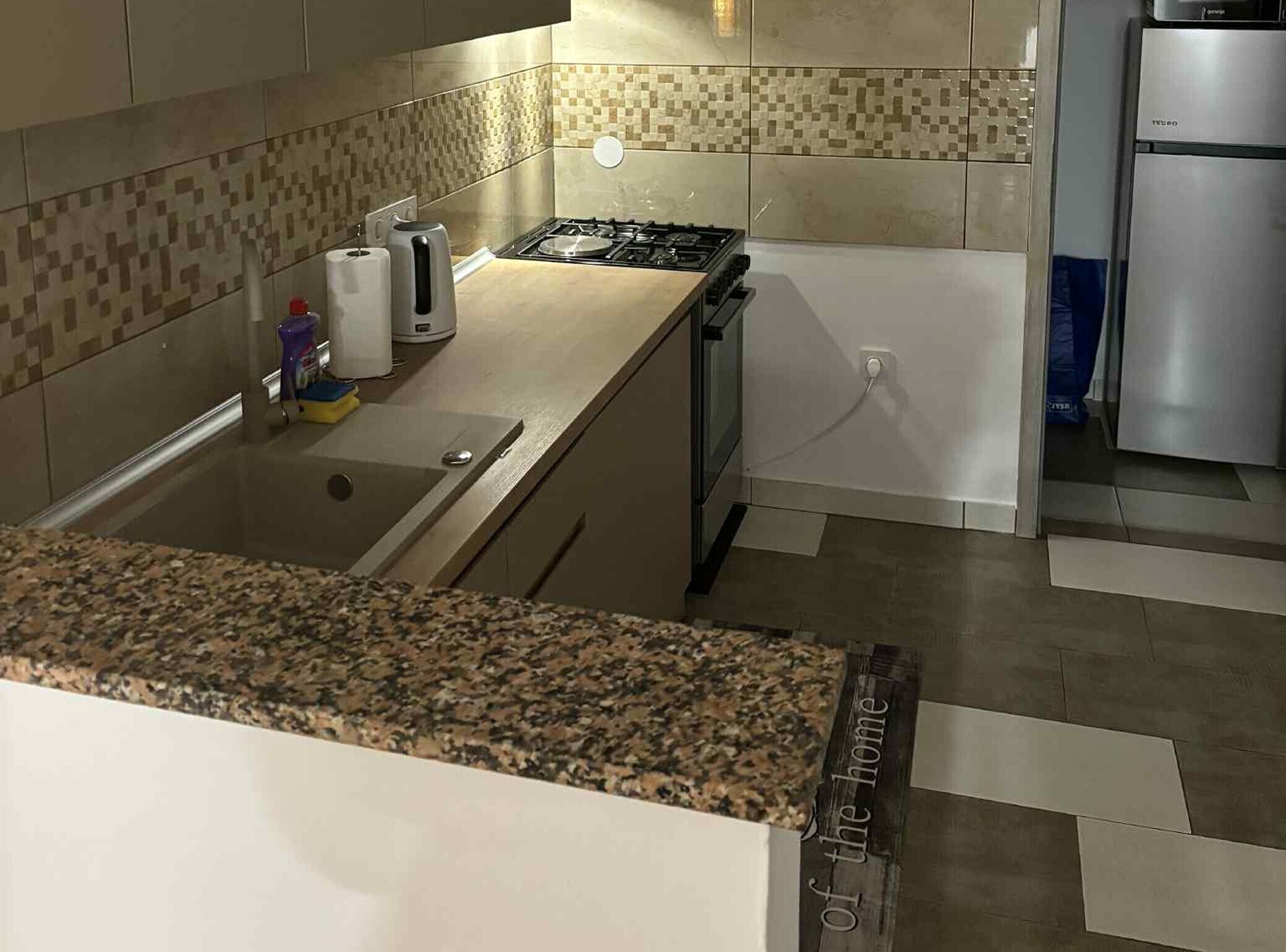 Eine Küche mit einer Granitabdeckung, einem Gasherd, einem Edelstahl-Kühlschrank und einer gefliesten Rückwand.