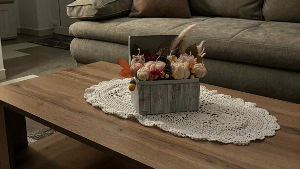 Una sala de estar con un sofá, una mesa de centro con una caja decorativa y un mantel de encaje.