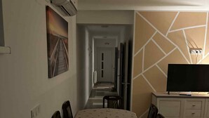 Habitación de hotel con comedor, televisor y pasillo que lleva a la salida.
