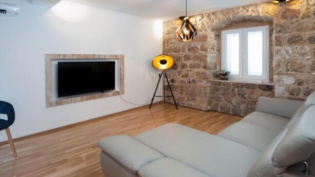 Un salon moderne avec un grand canapé, un téléviseur à écran plat, une lampe sur pied et un mur en pierre.