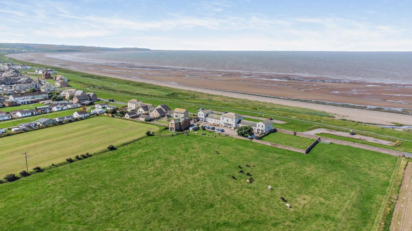 An aerial view of a coastal town with a beach, green fields, and residential buildings.
