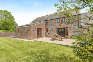 A stone house with a patio, a wooden table, and a door. - 4 Bed in St. Endellion (oc-t30725) (Trelights)